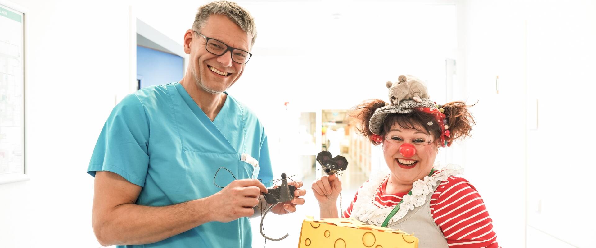 Freundlich lächelnder Arzt im türkisem Kittel mit Frau, die als Clown verkleidet ist und lalcht