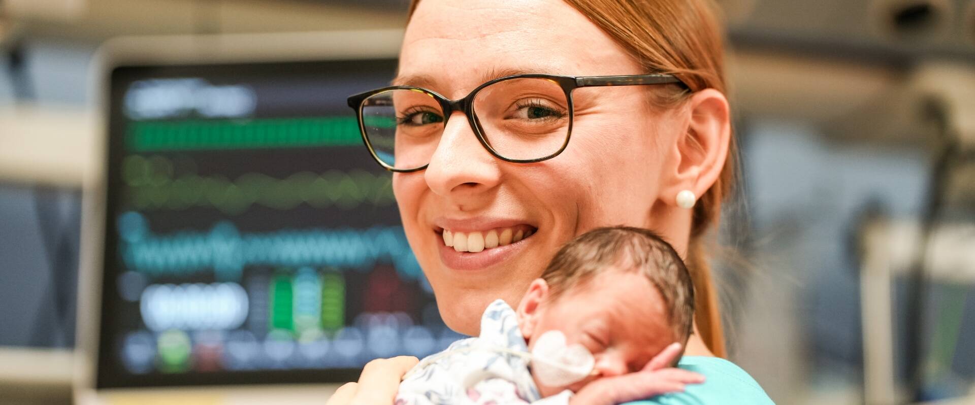 Junge Pflegerin, die sehr kleines Frühchen, dessen Kopf auf ihrer Schulter liegt, hält und lächelt