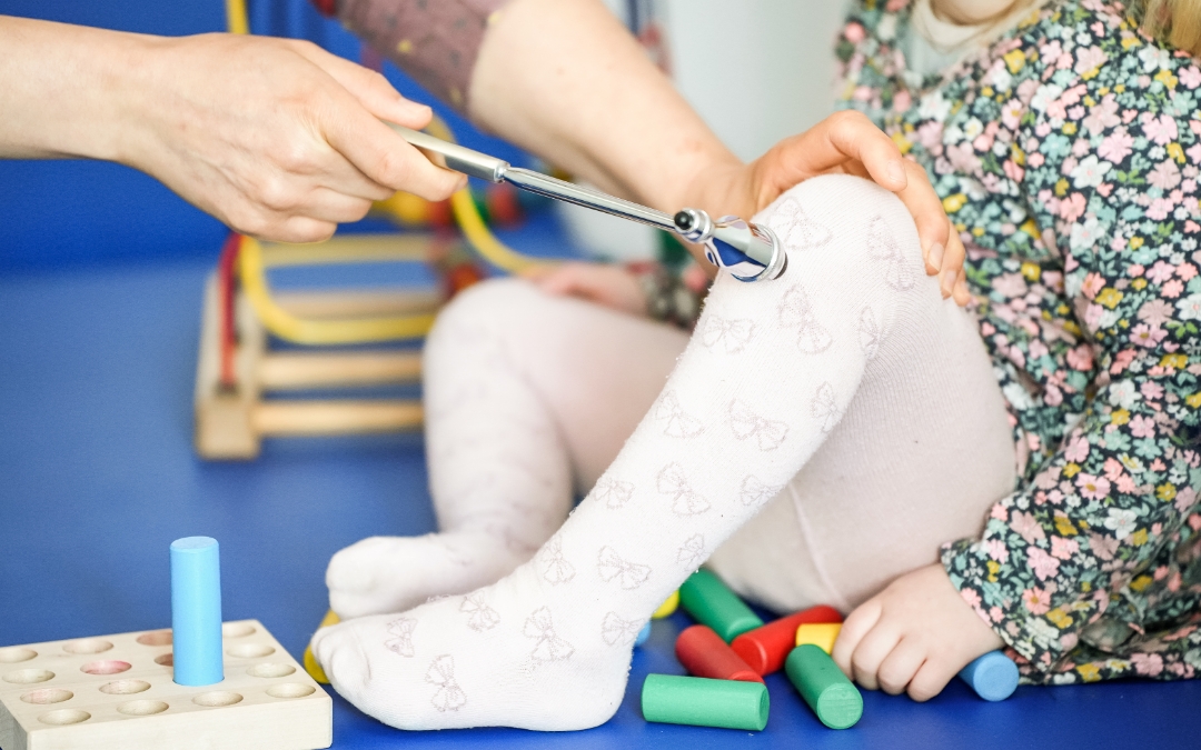 Beine eines kleinen Mädchens mit Strumpfhosen, deren Reflex am Knie mittel kleinem Hammer getestet wird